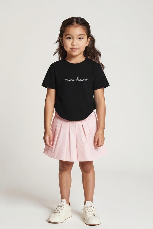 Young girl wearing a black t-shirt with text and a pink skirt on a white background